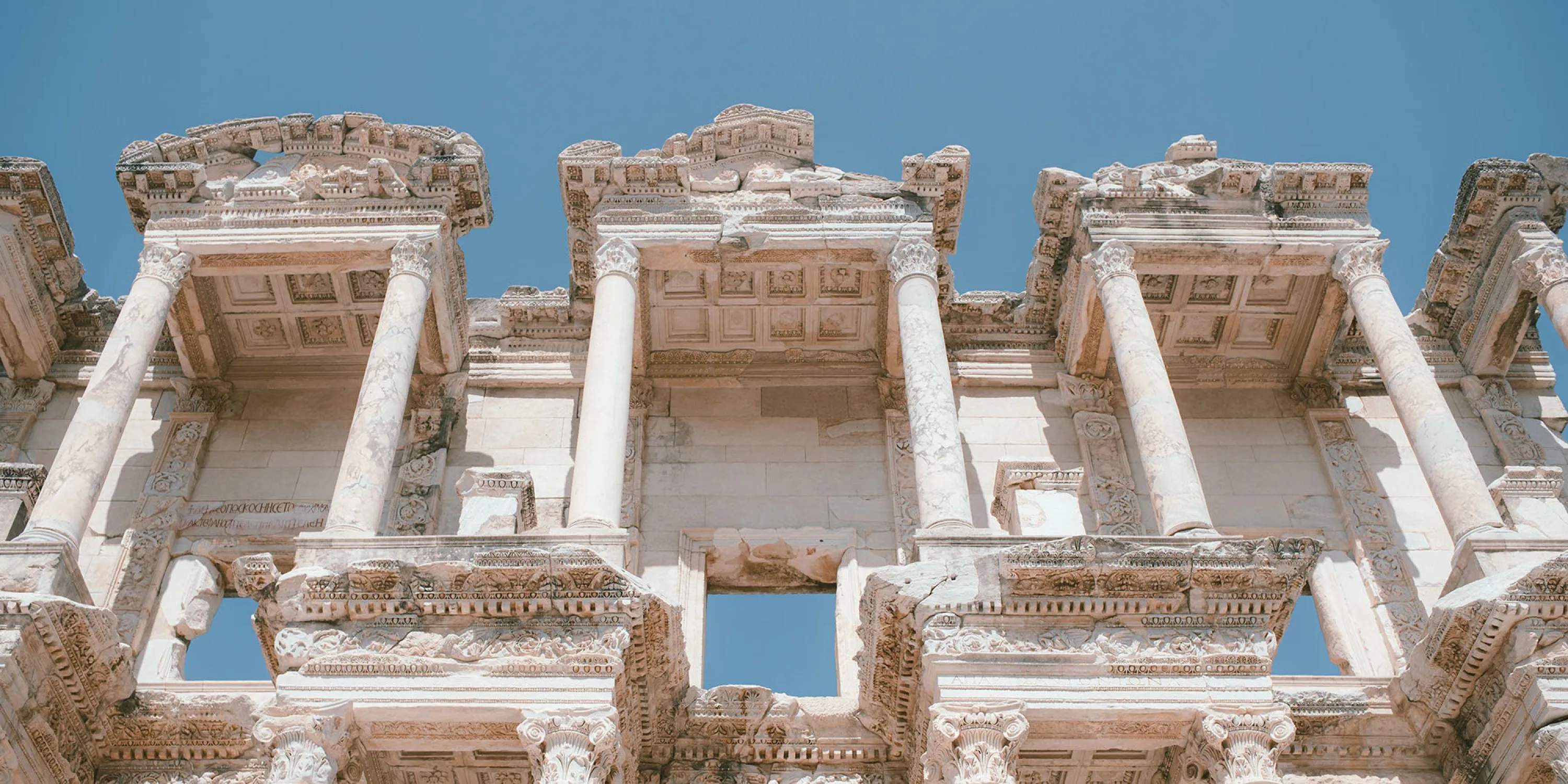 An image of the side of an ancient and intricately detailed building with blue sky in the background.