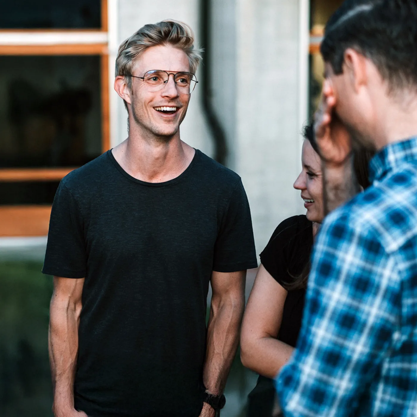 A male student wearing glasses and smiling at his peers.