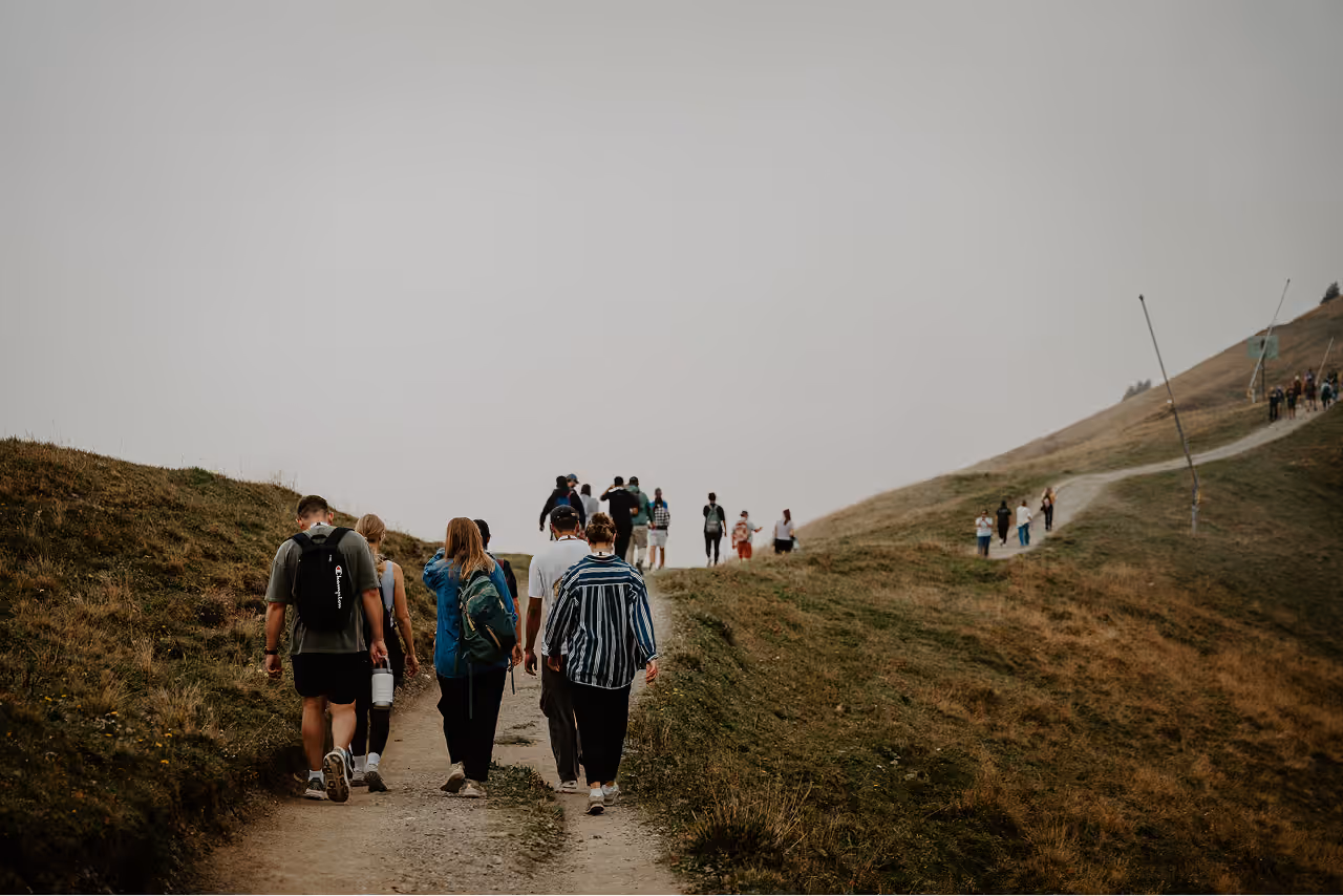 Group of people hiking on a dirt path through grassy hills under an overcast sky.